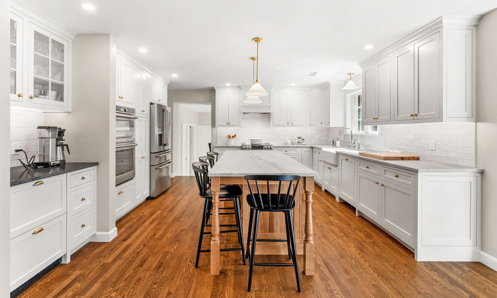 Modern remodeled kitchen with layered lighting, featuring recessed ceiling lights, pendant fixtures over a long white island, and warm hardwood floors.