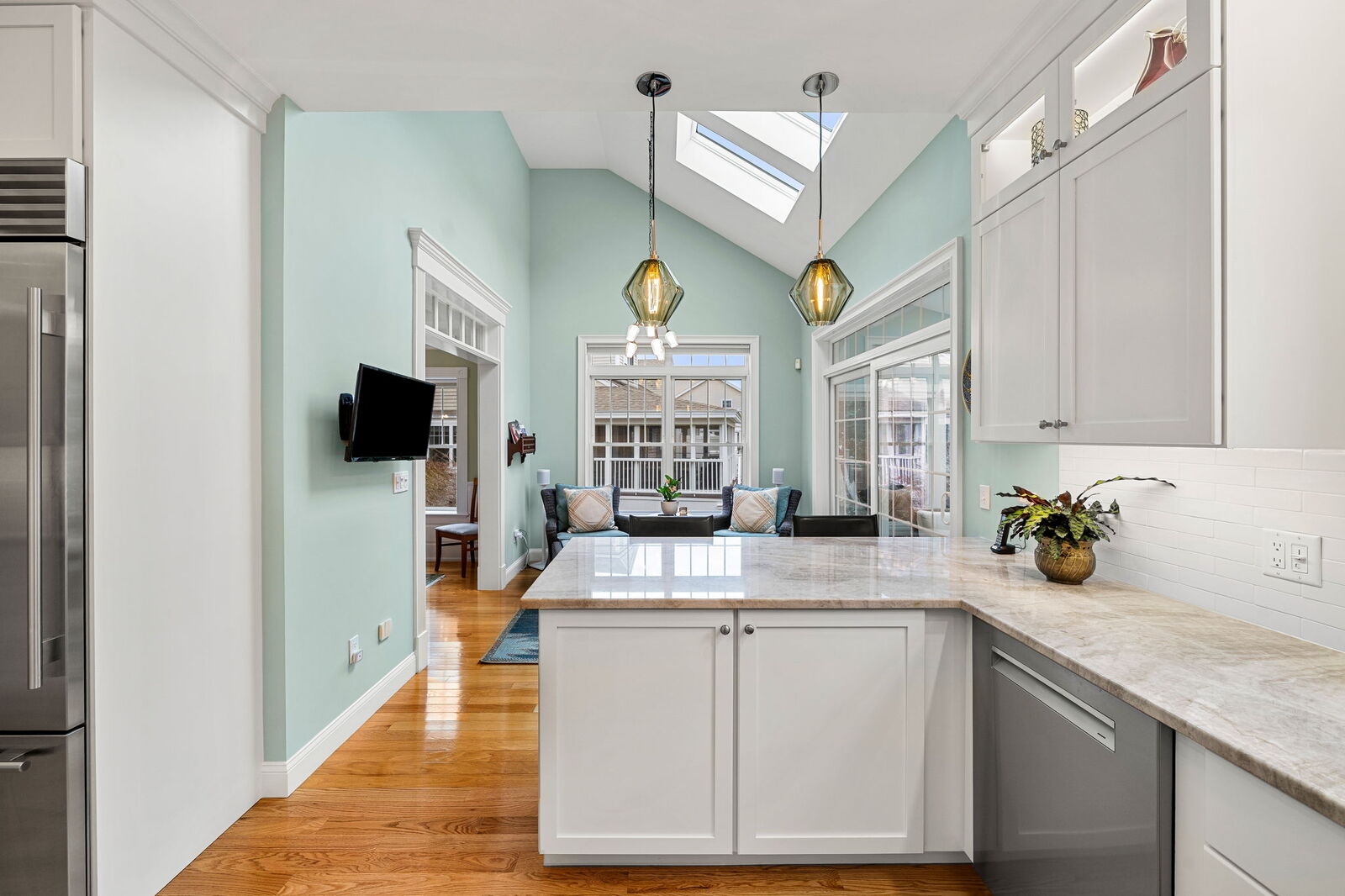 Remodeled coastal kitchen featuring skylights, light teal walls, white cabinets, hardwood floors, and pendant lights over a central island.